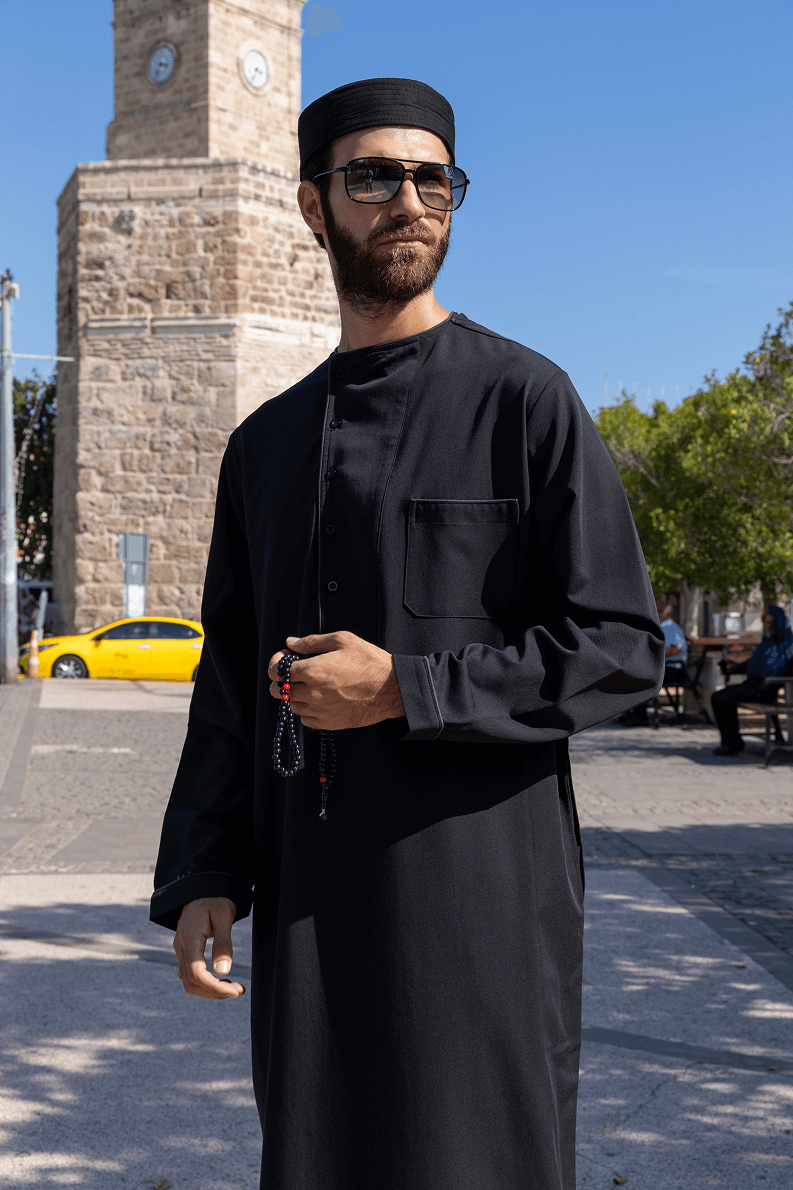 Man in a blue hooded robe holding glasses and a black bag against a white background.