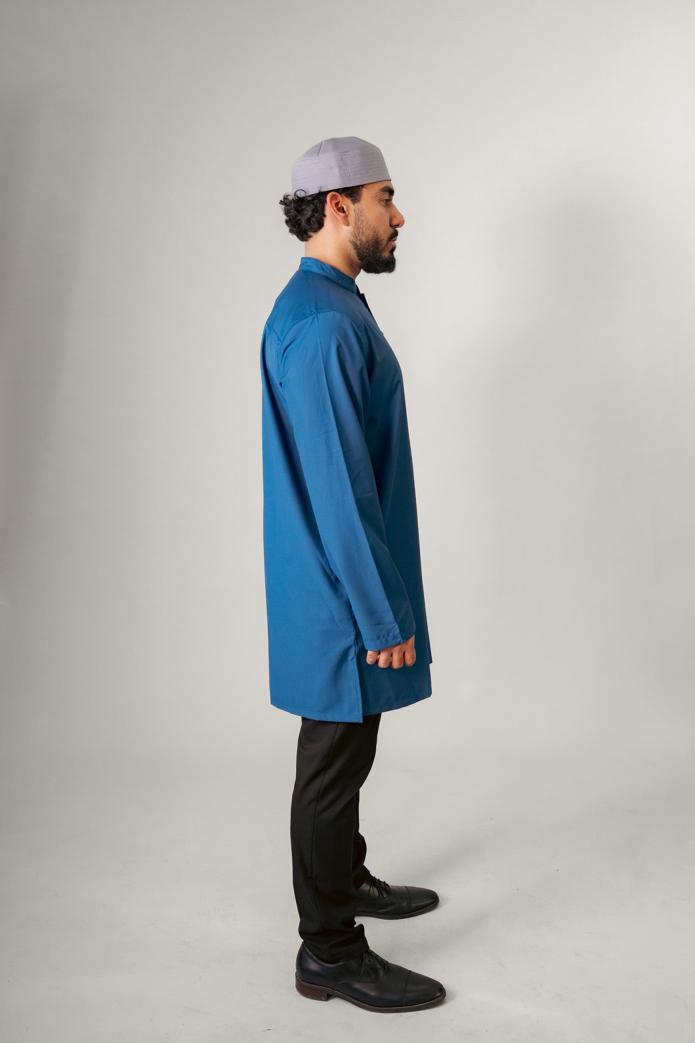 A person in a dark hooded robe, holding a string of beads, standing with back turned.