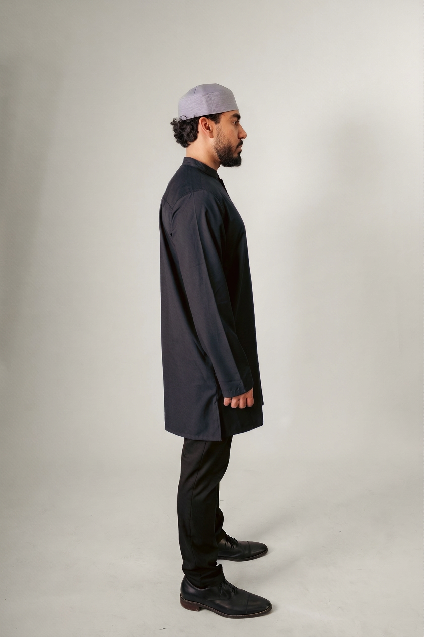 A person in a dark hooded robe, holding a string of beads, standing with back turned.