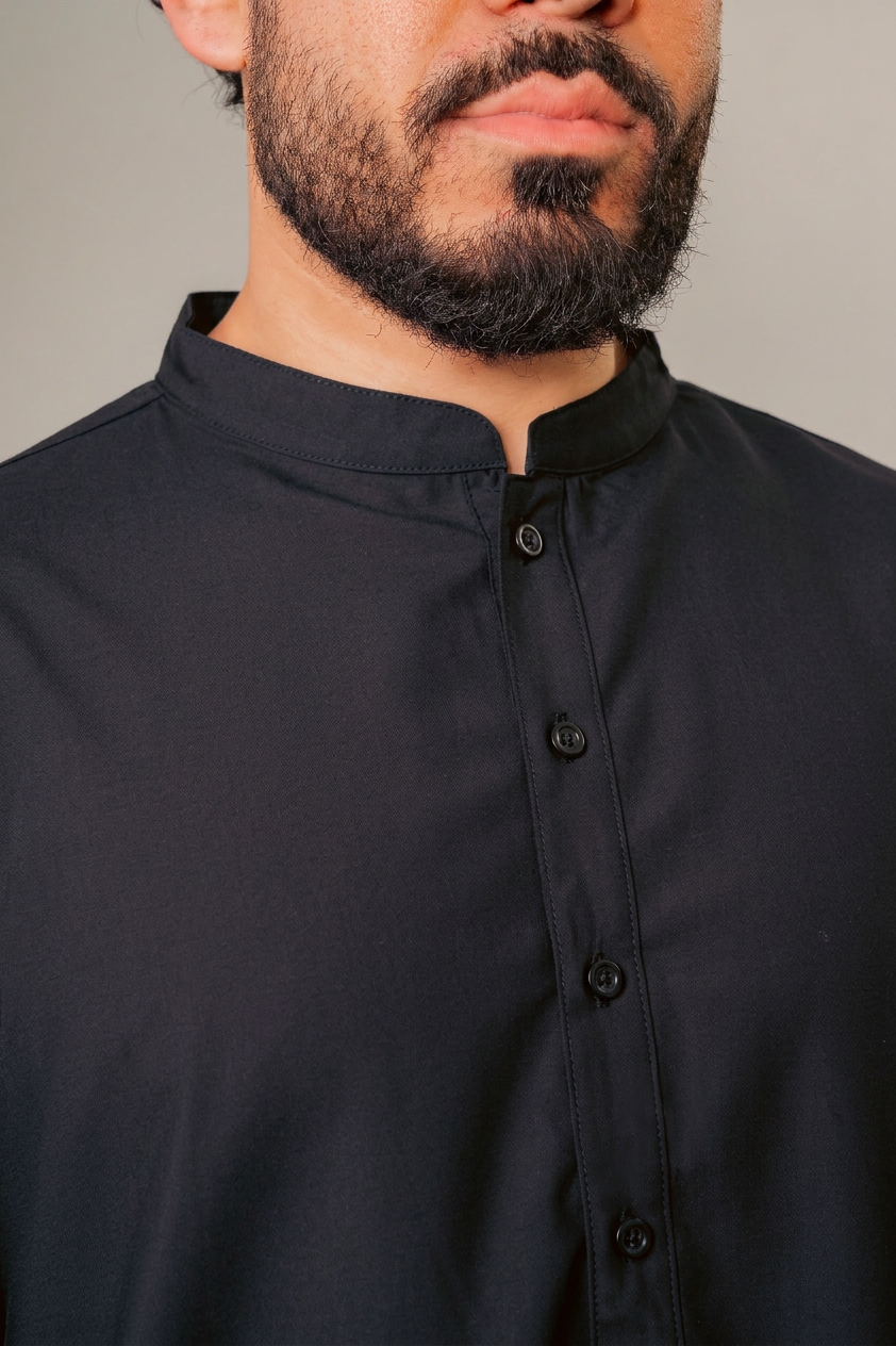Man in a blue hooded robe holding glasses and a black bag against a white background.