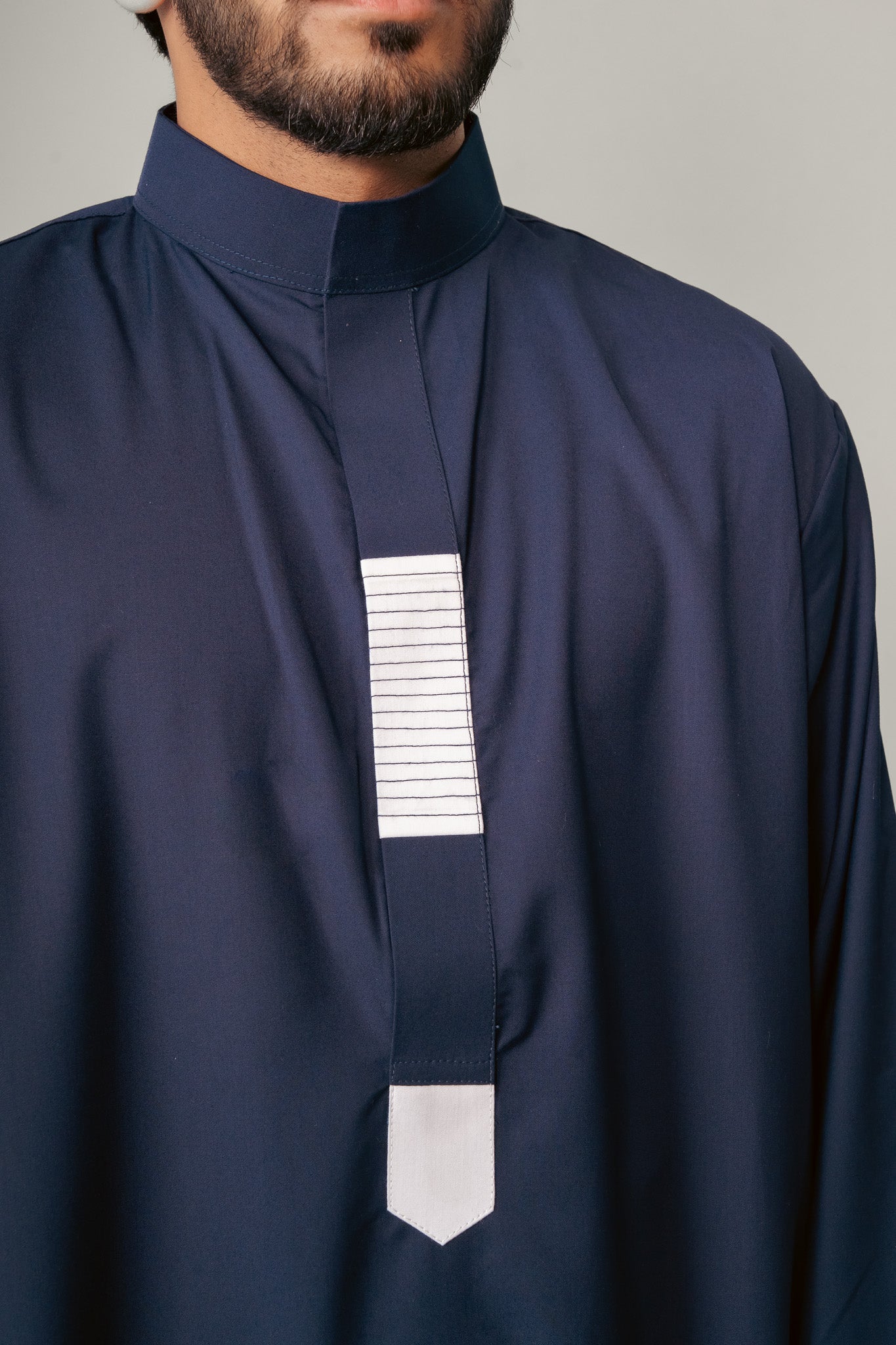 Man in a blue hooded robe holding glasses and a black bag against a white background.