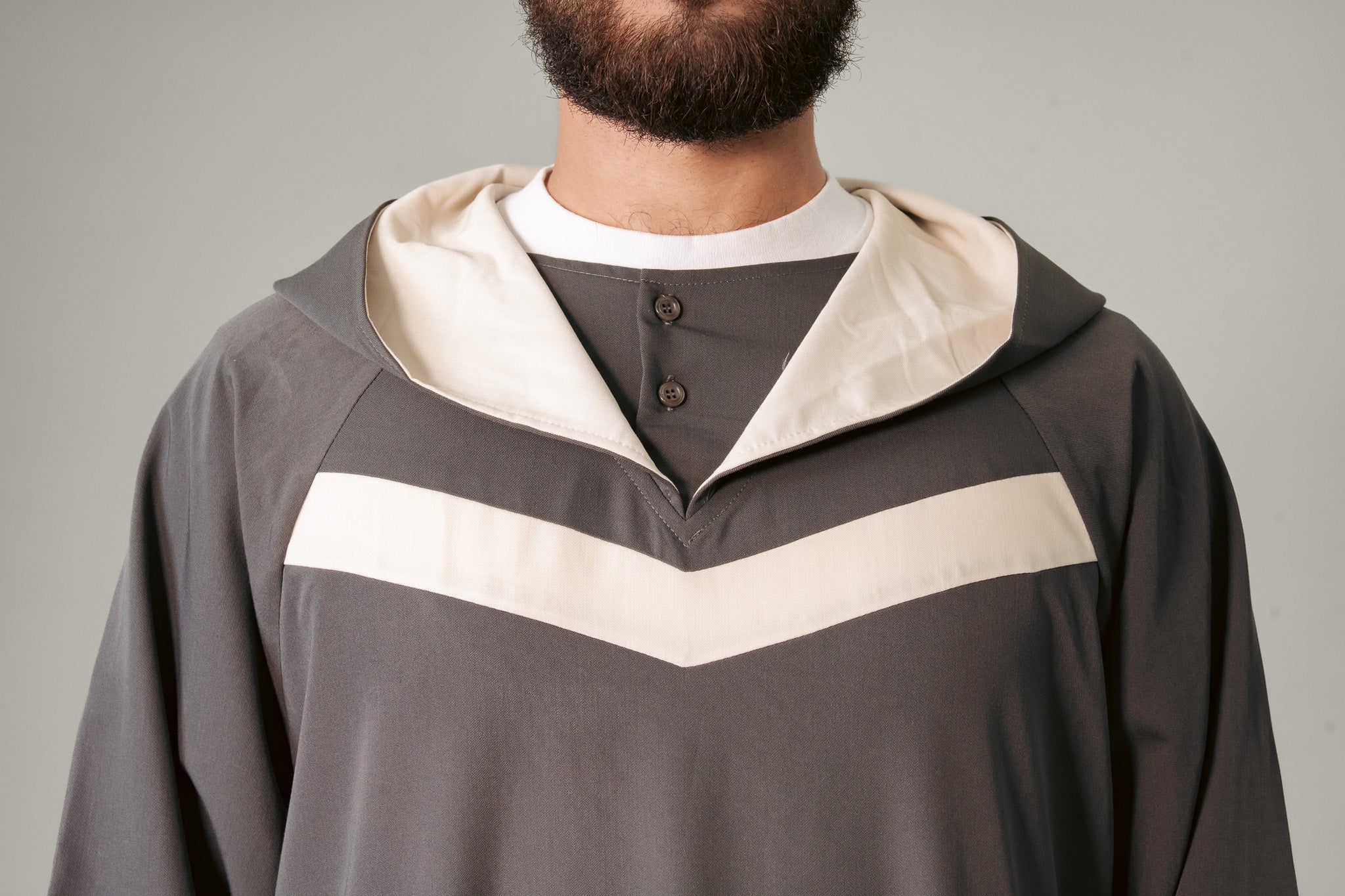 Man in a blue hooded robe holding glasses and a black bag against a white background.