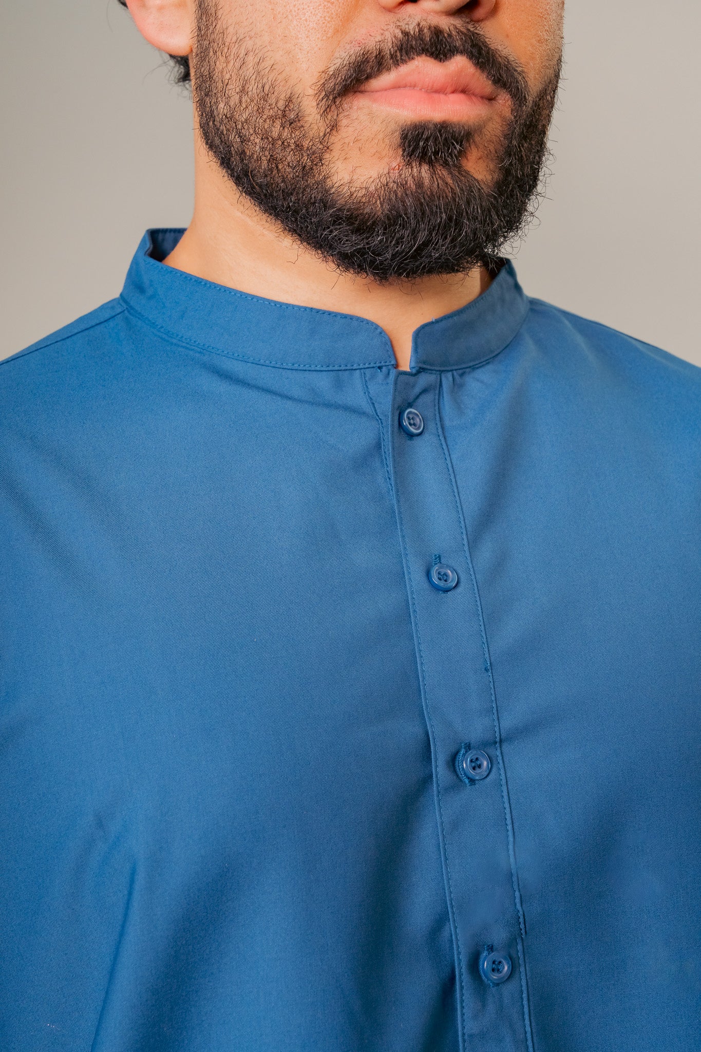 Man in a blue hooded robe holding glasses and a black bag against a white background.