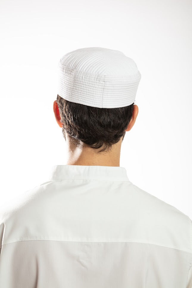 Man in navy traditional attire with hood, holding a beaded necklace, against a white background.