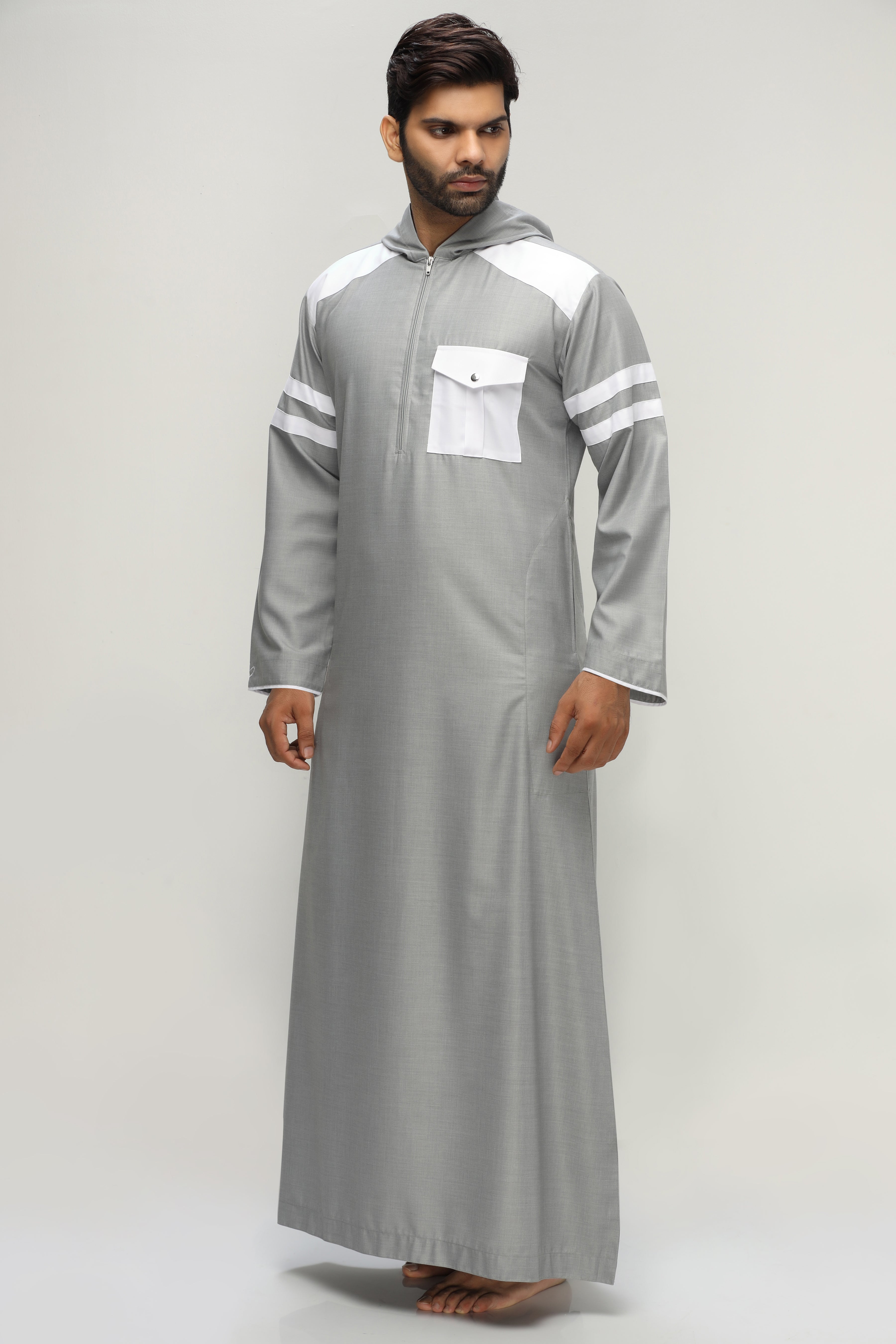 A person in a dark hooded robe, holding a string of beads, standing with back turned.