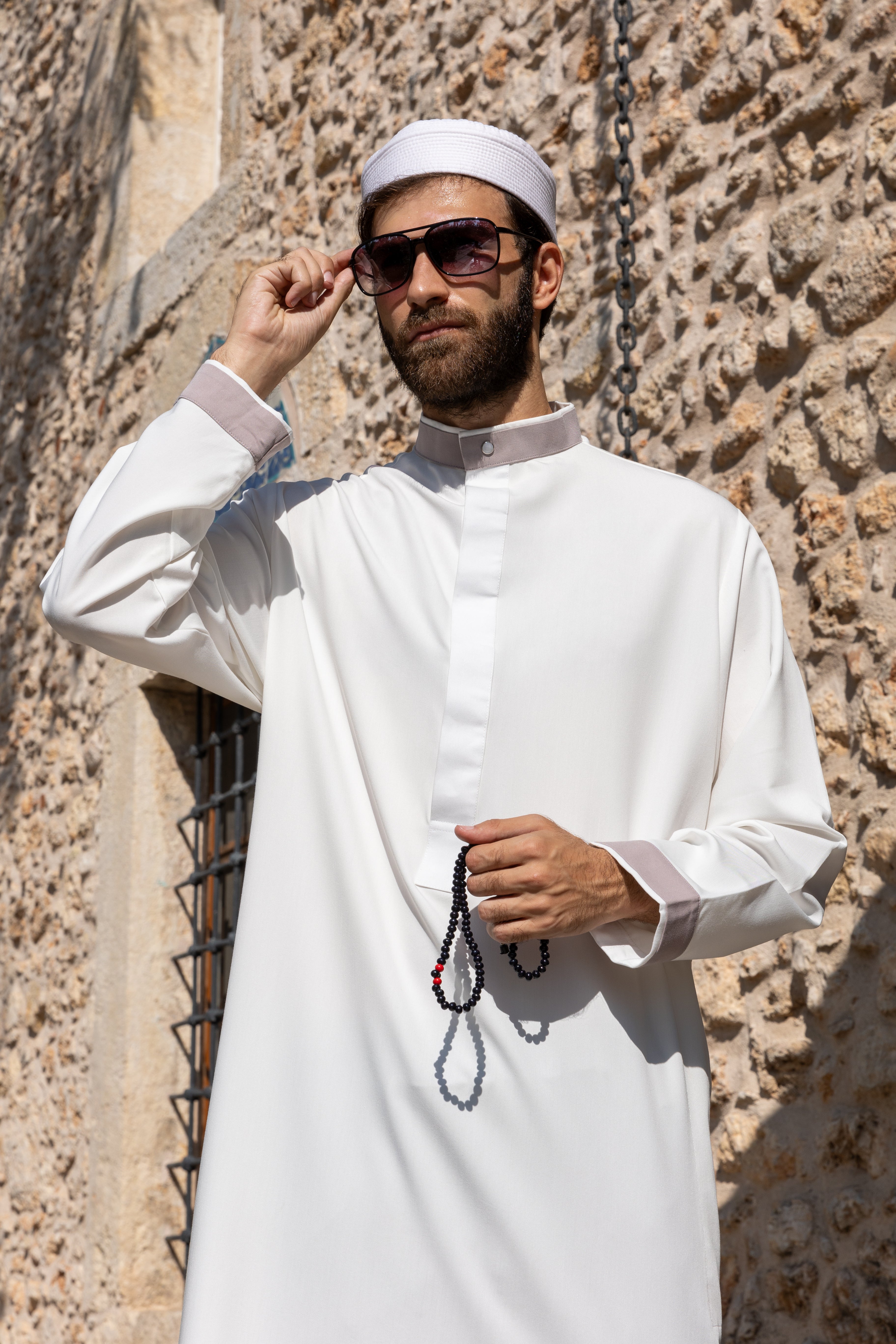 Man in a blue hooded robe holding glasses and a black bag against a white background.