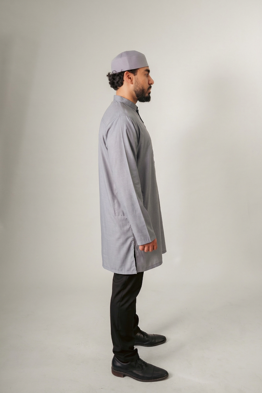 A person in a dark hooded robe, holding a string of beads, standing with back turned.