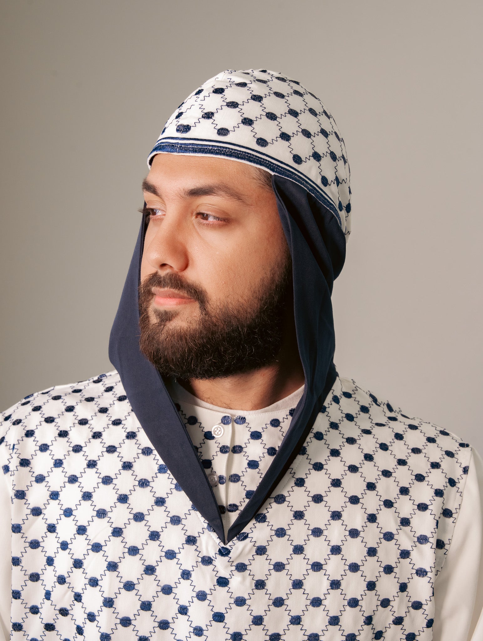 Man in a blue hooded robe holding glasses and a black bag against a white background.