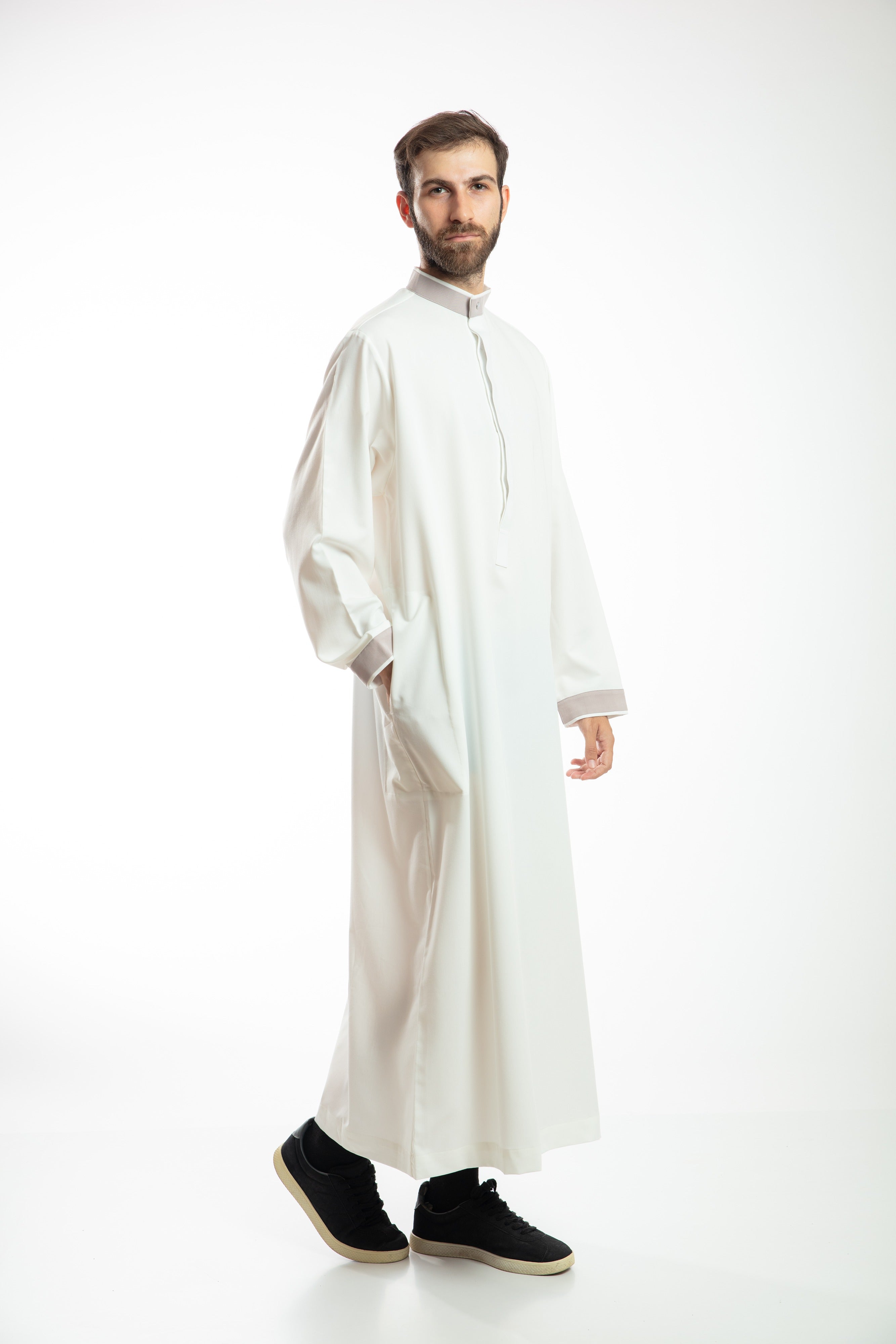 Man in navy traditional attire with hood, holding a beaded necklace, against a white background.