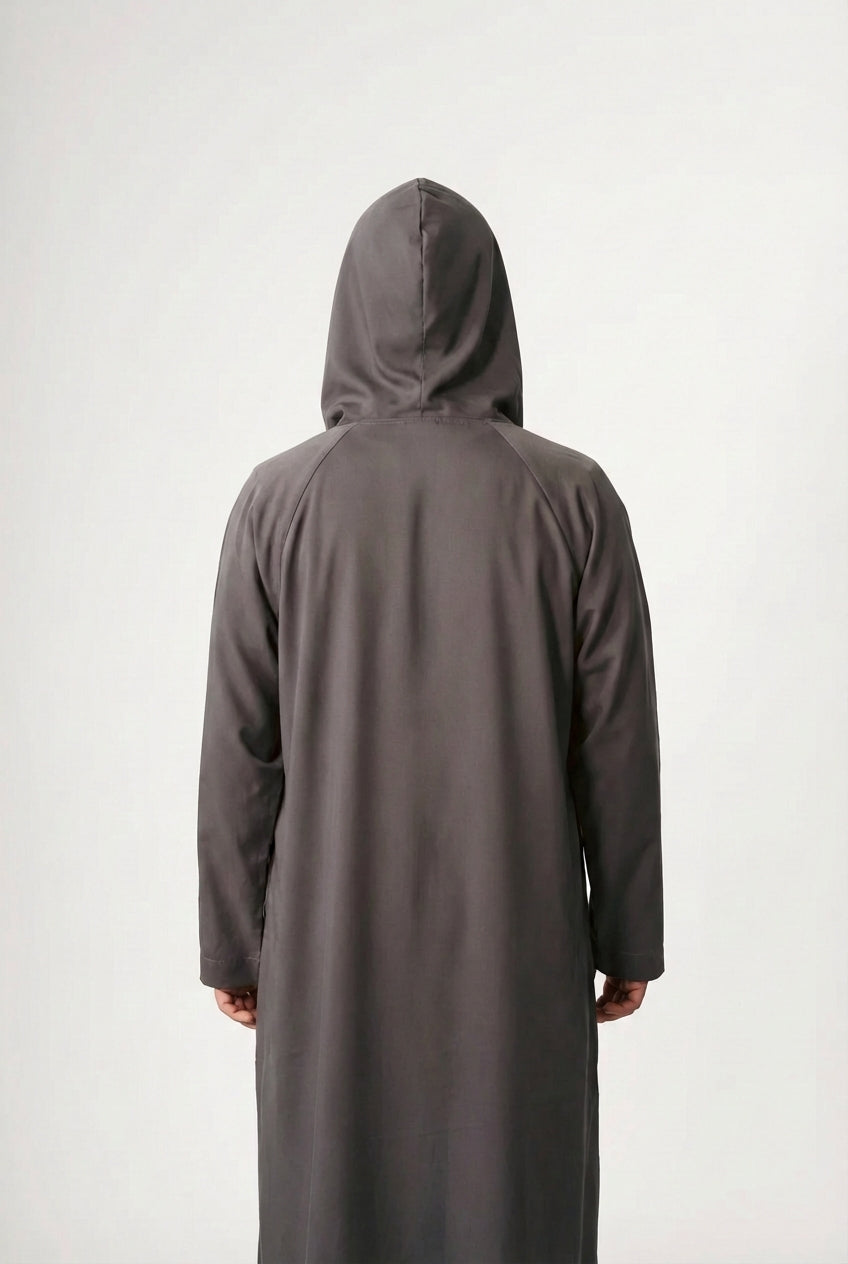 A person in a dark hooded robe, holding a string of beads, standing with back turned.