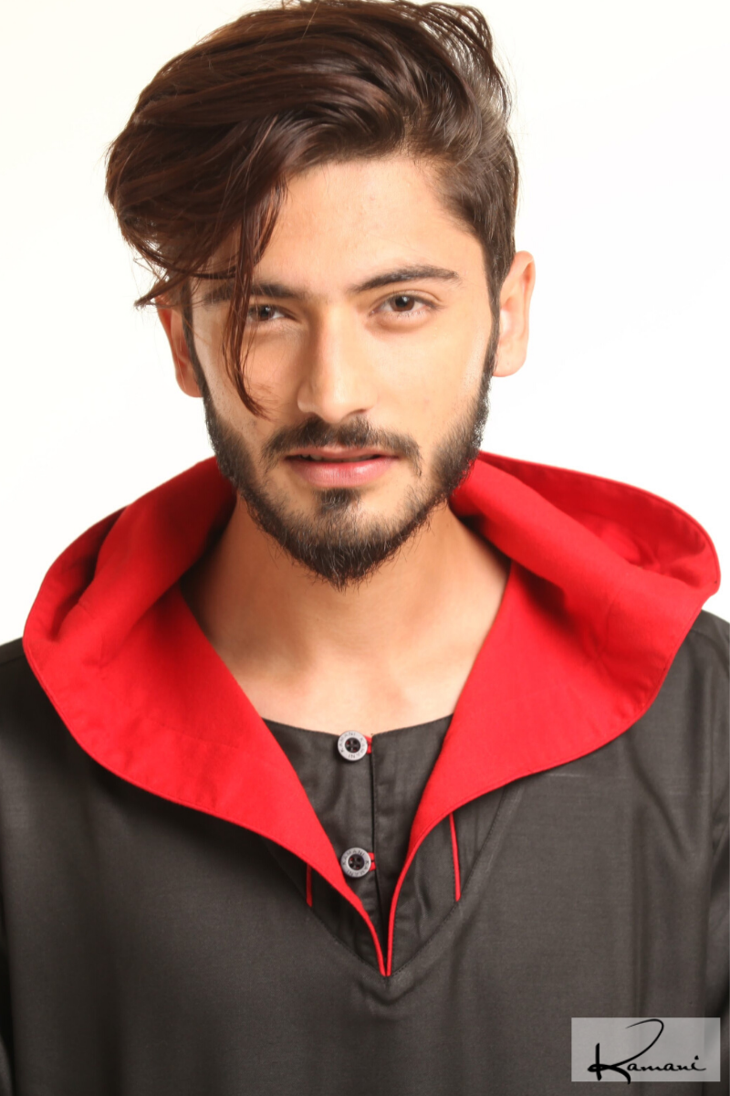 Man in navy traditional attire with hood, holding a beaded necklace, against a white background.